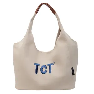 Minimalist beige canvas tote bag with blue embroidery and brown leather handle