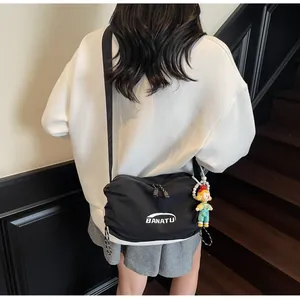 Detail of black nylon dumpling crossbody bag with adjustable strap and doll pendant