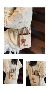 Detail of beige canvas tote bag with brown leather trim and heart charm on a wood staircase