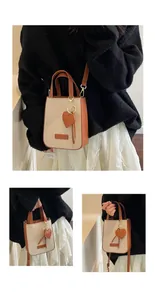 Detail of a beige canvas tote bag with brown leather trim and heart charm accessory