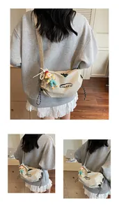 Detail of khaki nylon crescent bag with BANATU logo and decorative doll charm pendant