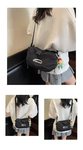 Detail of black nylon crossbody bag with BANATU logo and cute doll pendant on side
