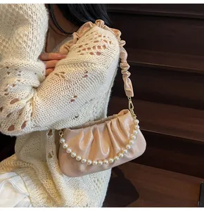 Detail der beige gefalteten Cloud-Bag mit Premium-Perlenkette und goldenen Metallbeschlägen