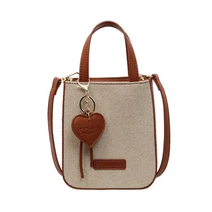 Fashionable beige denim canvas and brown leather crossbody bag with heart charm