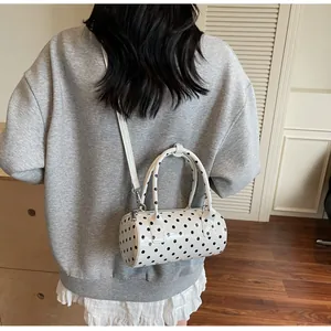 Polka dot cylinder crossbody bag styled on shoulder in a minimalist indoor setting