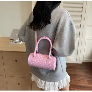 Pink polka dot cylinder Boston bag shown on a shoulder in a cozy indoor setting