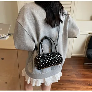 Close-up of a black glossy polka dot duffel bag with handles and a long shoulder strap