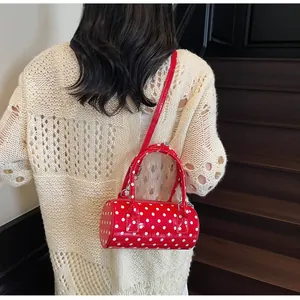 Polka dot red cylinder handbag shown cross-body with glossy finish and strap