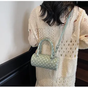 Polka dot cylinder handbag in light green with adjustable strap shown on model shoulder