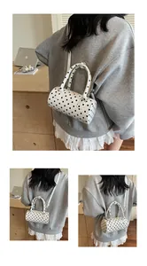 Detail of white polka dot cylinder crossbody bag with double handles and shoulder strap