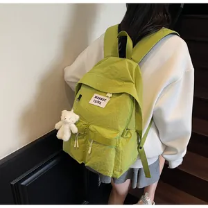 Close-up of avocado green nylon backpack featuring white logo patch and plush bear charm
