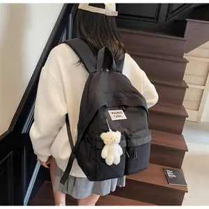 Detail of black nylon backpack with fluffy bear pendant and minimalist lettered patch