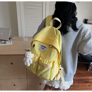 Detail view of a yellow nylon backpack with multi-pockets and a cute white bear keychain