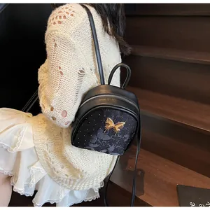 Detalle de una mini mochila negra con adorno de mariposa plateada y textura floral en relieve