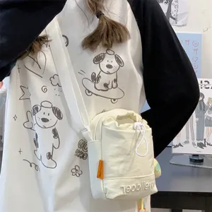 Detail van beige crossbodytas met trekkoord, oranje zijlabel en geborduurde letters