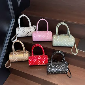 Cylindrical polka dot handbags in six shiny colors displayed on wooden stairs