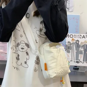 Detail van de gebroken witte canvas crossbodytas met trekkoord en merkborduurwerk