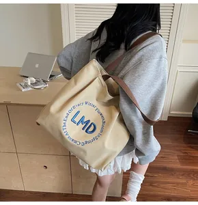 Detail of a beige canvas tote bag with brown shoulder straps and blue circular embroidery