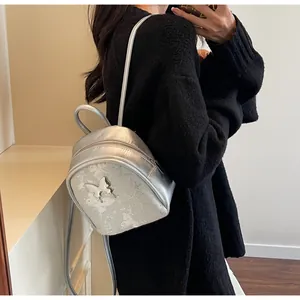 Mochila mini plateada con mariposa mostrada en la espalda de la modelo a la moda