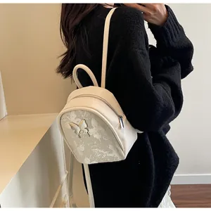 Vista detallada de la mini mochila crema con mariposa de metal 3D y patrón de mármol