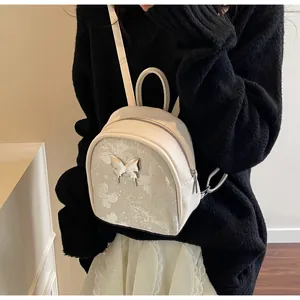 Primer plano de mini mochila color crema con detalles de mariposa plateada y asas
