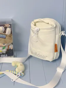 Detail van gebroken witte crossbodytas met trekkoord, borduursel en oranje label