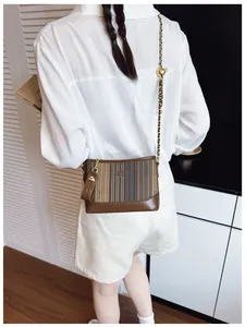 Gros plan du sac bandoulière marron rayé avec chaîne dorée et logo COI ZDN