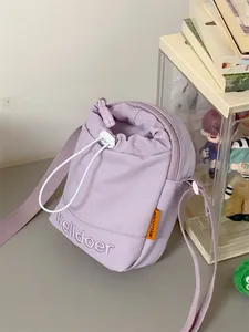 Detail van lichtpaarse nylon crossbodytas met trekkoordsluiting en oranje merklabel