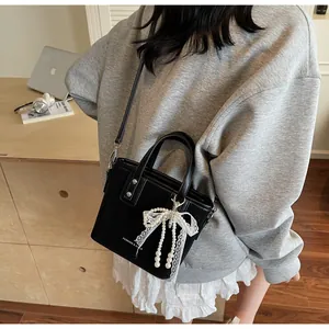 Detail of black bucket bag with white lace bow, pearl charms and metal rivets