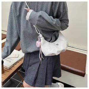 Weiße Halbmond-Tasche mit dünnen Trägern und rosa Herzanhänger in einer Café-Szene