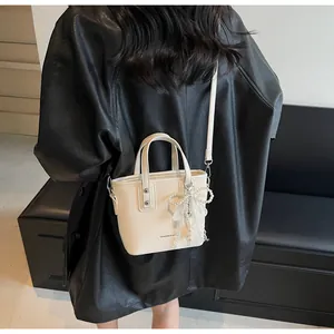 Detail of cream mini bucket bag with pearl lace bow and detachable shoulder strap on model