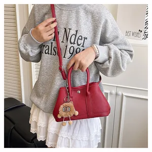 Detail der roten Handtasche aus Leder mit Litschimuster und süßem Löwen-Plüsch-Anhänger