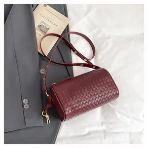 Detail of burgundy woven cylinder bag with gold hardware on a gray blazer and white fabric