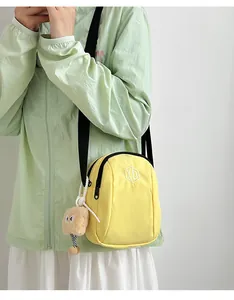 Dettaglio della borsa a conchiglia in nylon giallo con logo ricamato e ciondolo
