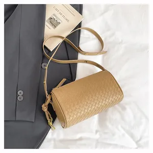 Detail of tan woven cylinder crossbody bag with golden hardware and textured finish