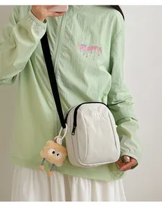 Dettaglio di una borsa a tracolla in nylon crema con tracolla regolabile e logo geometrico