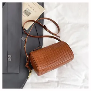 Detail of a brown woven cylinder bag with gold rivets on a stylish shoulder strap