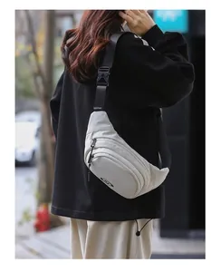 Outdoor shot of an off-white crossbody bag with adjustable strap and multiple zippers