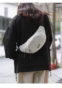 Outdoor street view of a beige SLE crossbody bag showing size and fit on a model