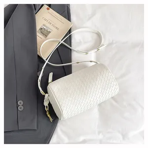 Close-up of white woven PU leather cylinder bag with gold hardware on fabric