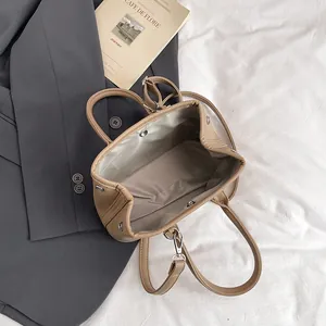 Schicke khakifarbene Schultertasche aus genarbtem Leder auf Bettwäsche mit Accessoires