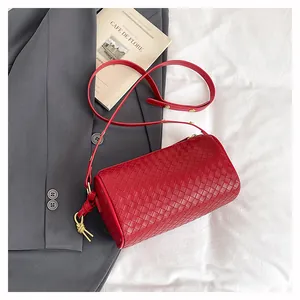 Macro shot of red woven leather cylinder bag with gold knot hardware on fabric