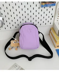 Dettaglio della borsa a conchiglia in nylon lilla con logo ricamato e ciondolo di peluche