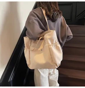 Detail of a large beige canvas tote bag with functional pockets and a sturdy shoulder strap