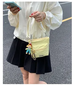 Detailed outdoor shot of a light yellow nylon bucket bag with cute doll charm and thick strap