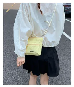 Outdoor shot of light yellow nylon crossbody bag with chic buckle and zipper pocket