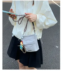 Detail of light gray nylon bucket bag with bicolor rope strap and cute doll charm