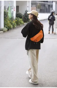 Outdoor street view of a bright orange canvas crossbody waist bag worn by a model