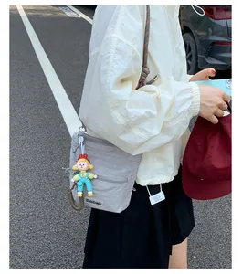 Detail of grey nylon crossbody bag with chic zipper pockets and a cute cartoon doll pendant