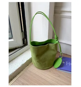 Close-up of green suede bucket bag featuring leather trim and round coin purse charm